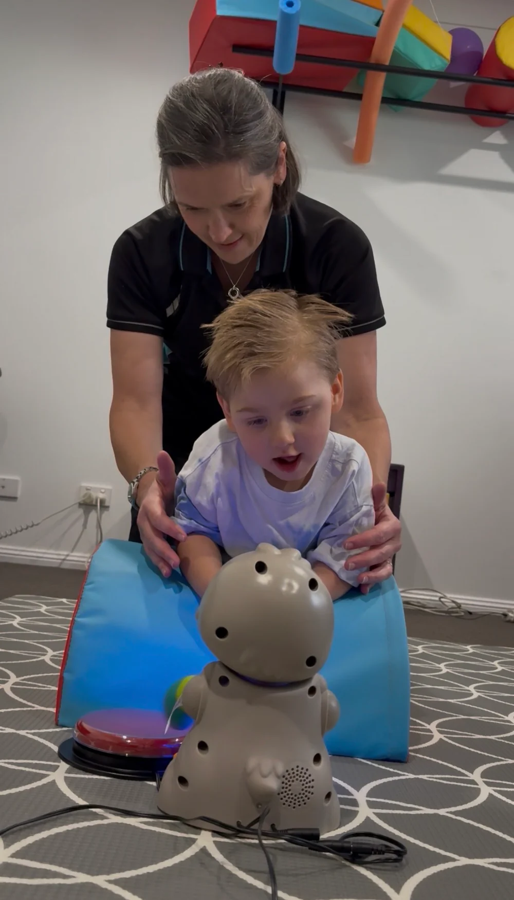 A physio supporting a child on their tummy over a foam wedge