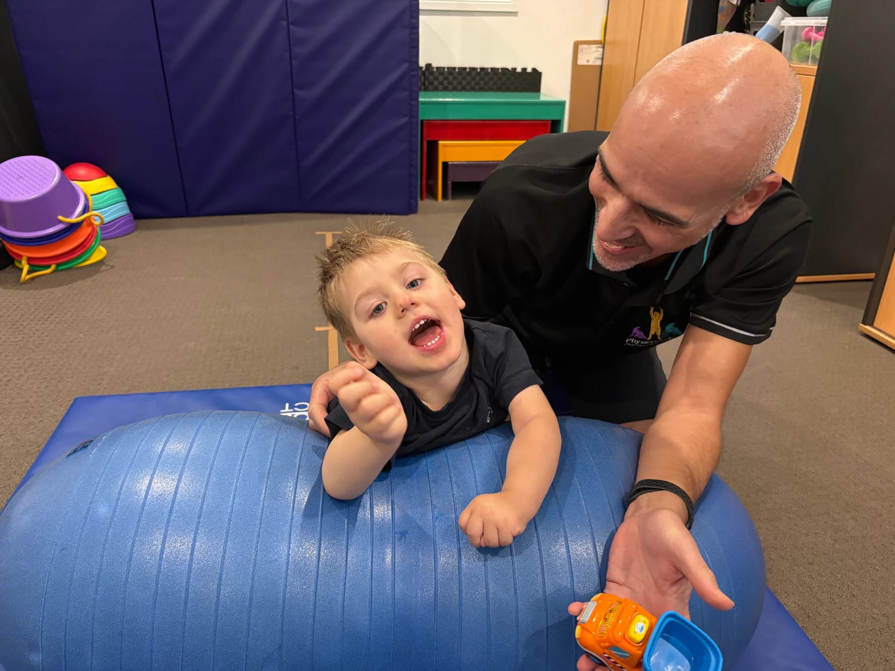 A physio supporting a laughing toddler on a peanut ball