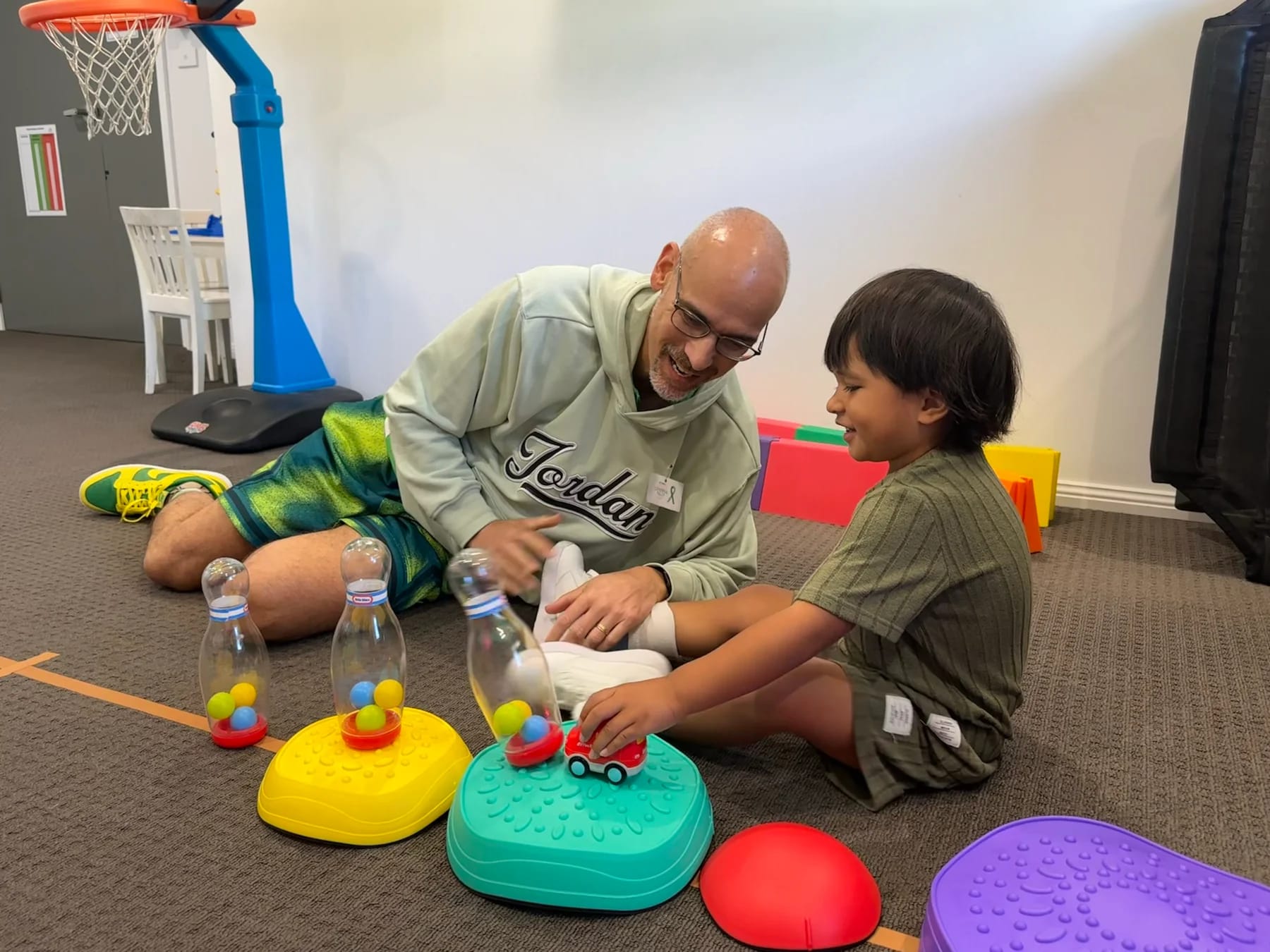 A physio and a boy sitting on the floor playing with a toy truck and skittles