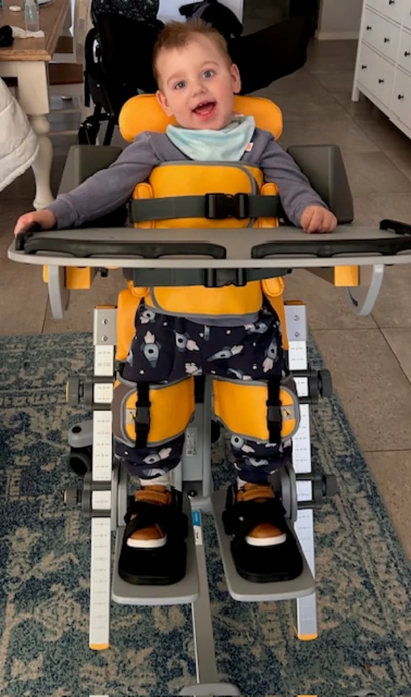 A smiling toddler supported in a standing frame